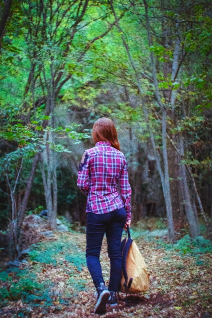 A girl with an orange backpack in her hand standing on a trail in the woods