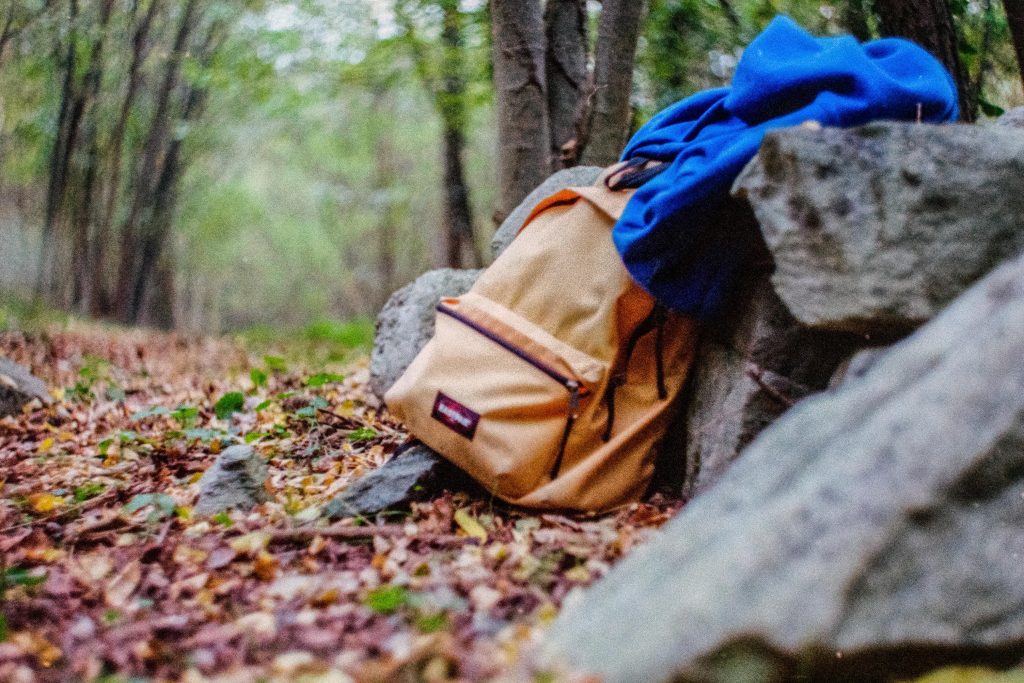 An orange backpack and a blue jacket on a dry wall made of rocks on the side of a trail in the woods 