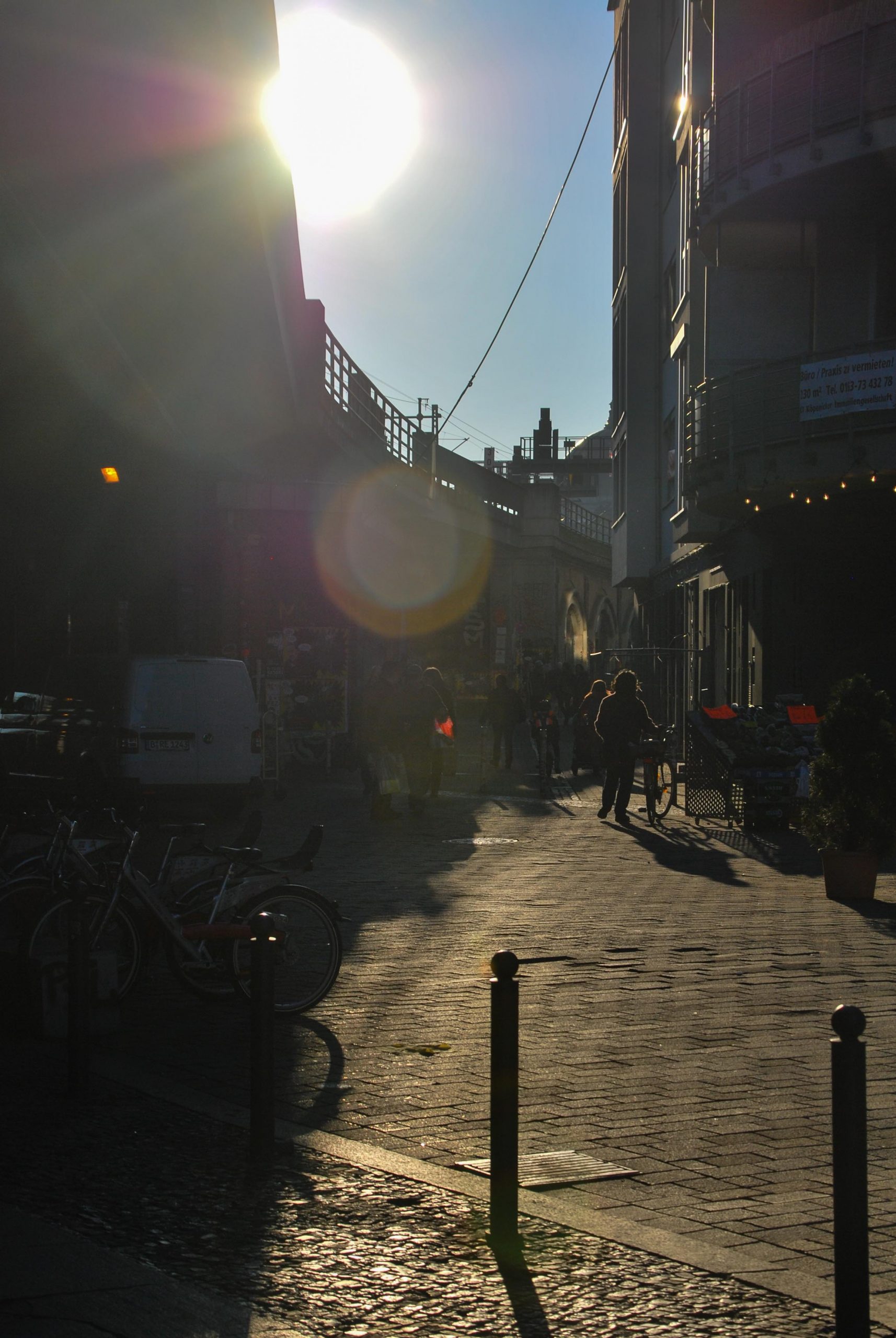 Una via con delle persone, un po' in ombra e un po' al sole