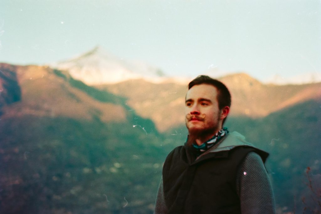 A guy standing in front of the camera with sunsetting mountains in the background