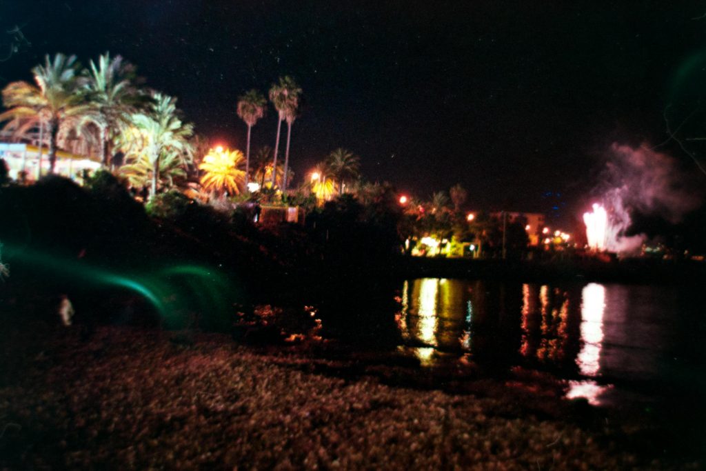 A Night view of the city lights of San Remo with fireworks in the background, shot from a beach 