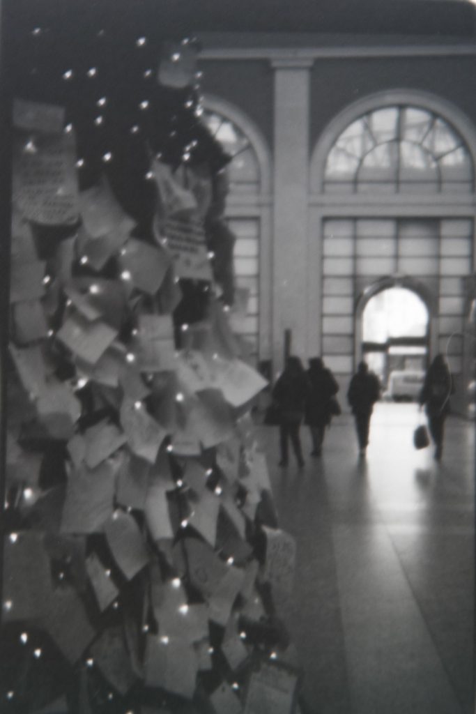 A christmas tree inside a train station with a lot of post-its with wishes written on them 