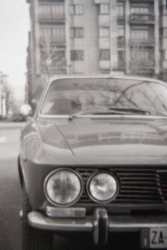 a Black and white photo representing The front of an Alfa Romeo GTV woth its Headlights near the camera