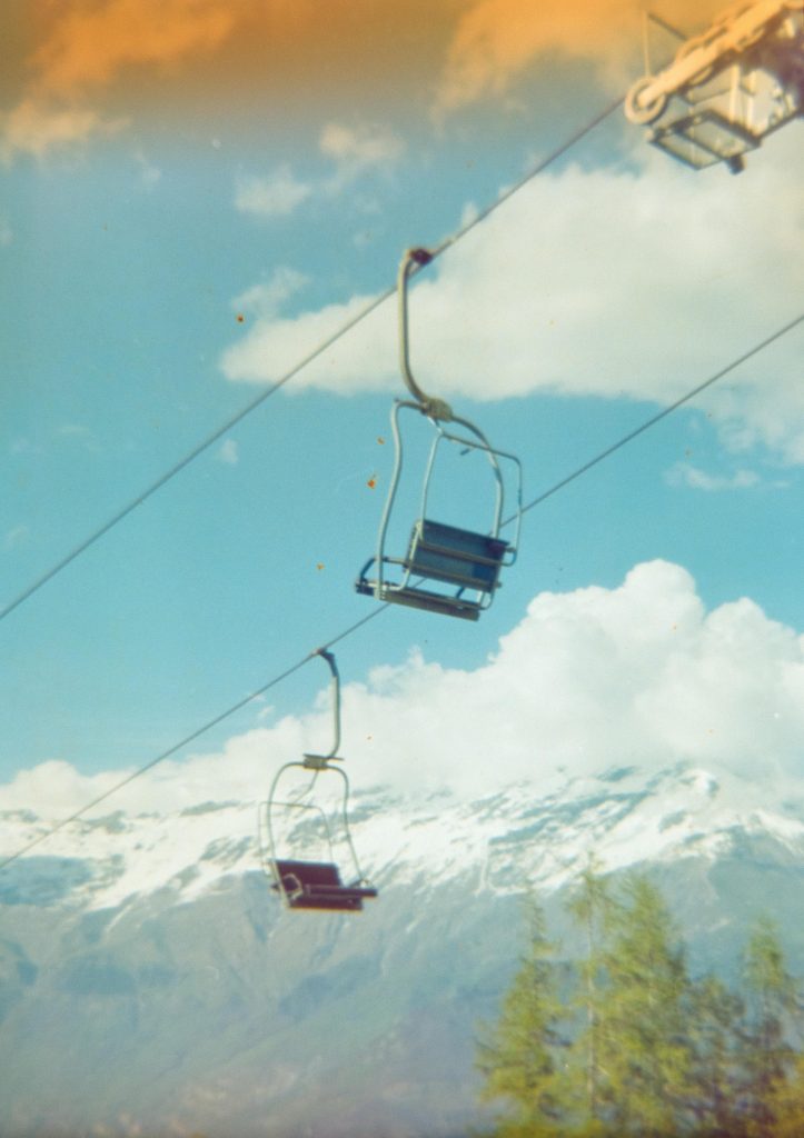 A couple of chairlift seats hanging still with some mountains and a blue sky with white clouds in the background