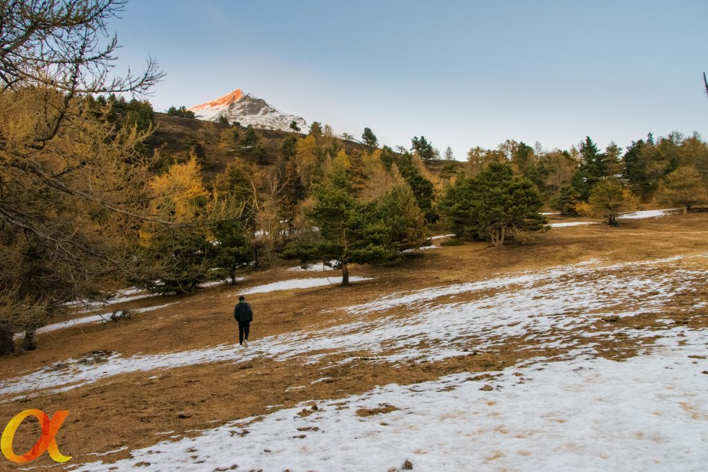 Paesaggio di montagna con una persona che cammina in un prato parzialmente coperto di neve