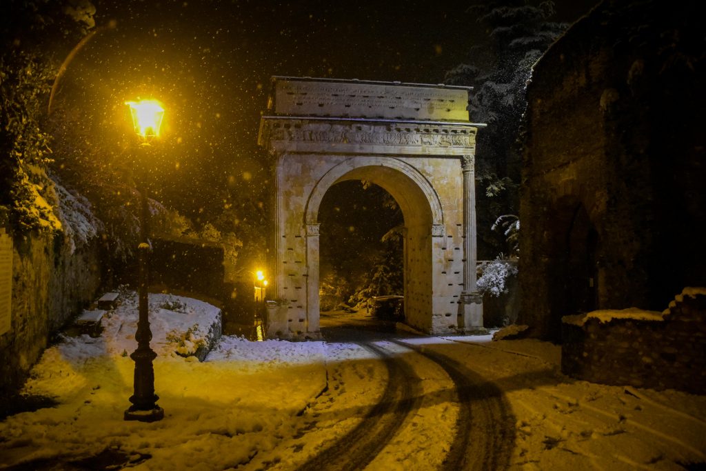 Foto di un arco romano innevato di sera