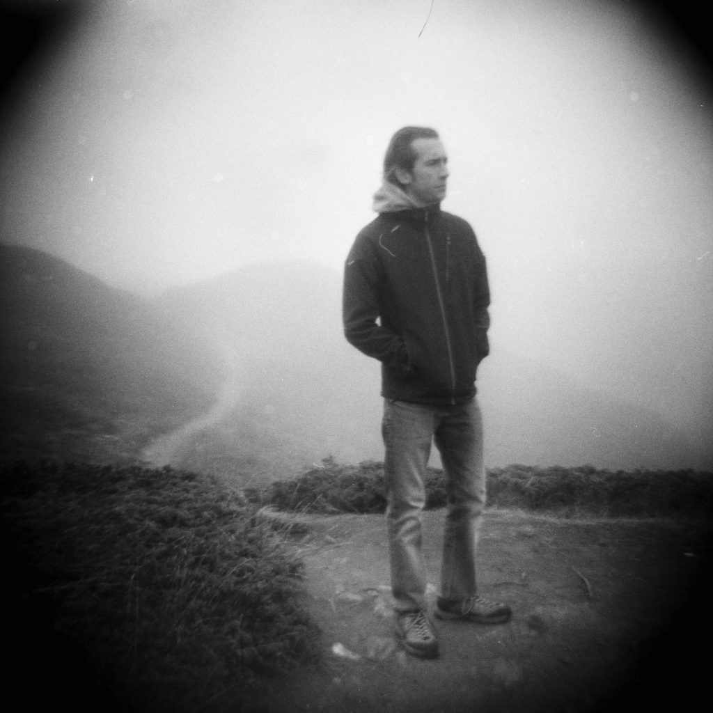 a person standing in front of a single track path in a hilly background