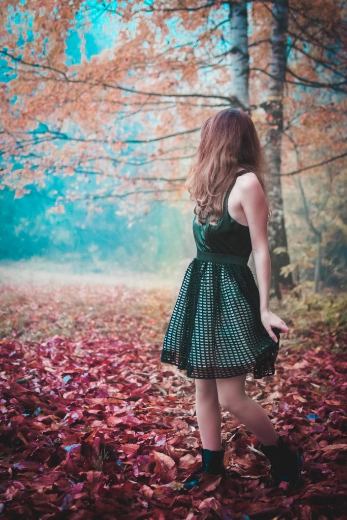 A girl in a black dress standing in a Fall-sy wood scenery