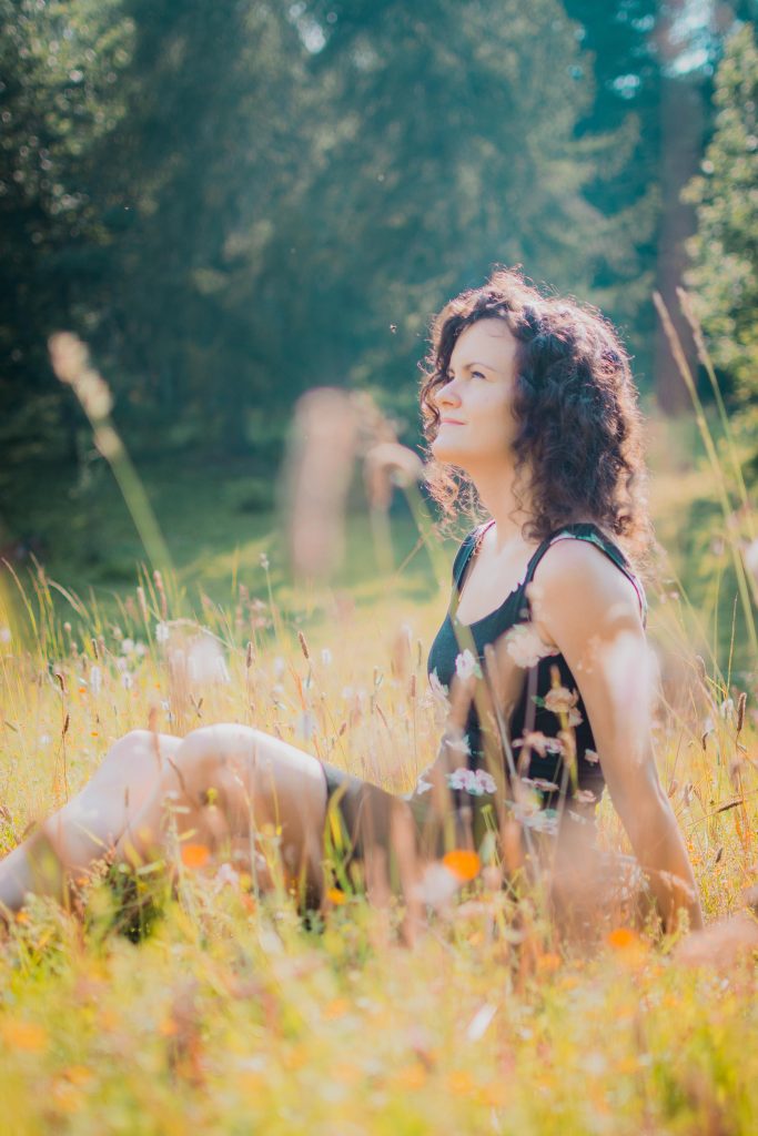 a girl with a black sleeveless dress sitting in a field in the woods