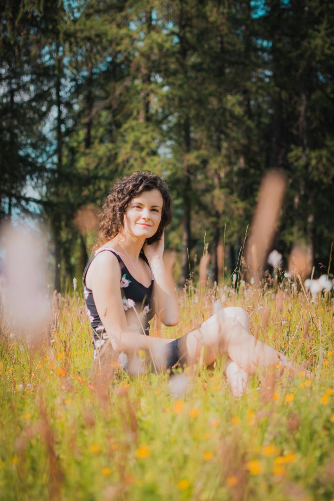 A girl with a black sleeveless dress sitting in a field in the woods 