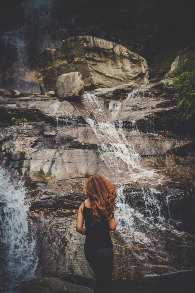 A girl with red curly hair standing in front a waterfall