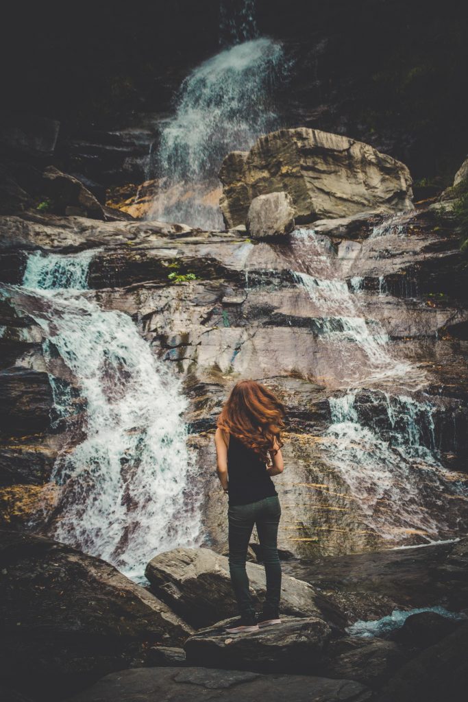 A girl with red curly hair standing in front of a waterfall