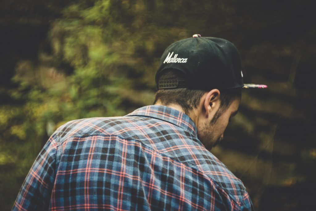 A guy with a hat and a flanel seen from the back