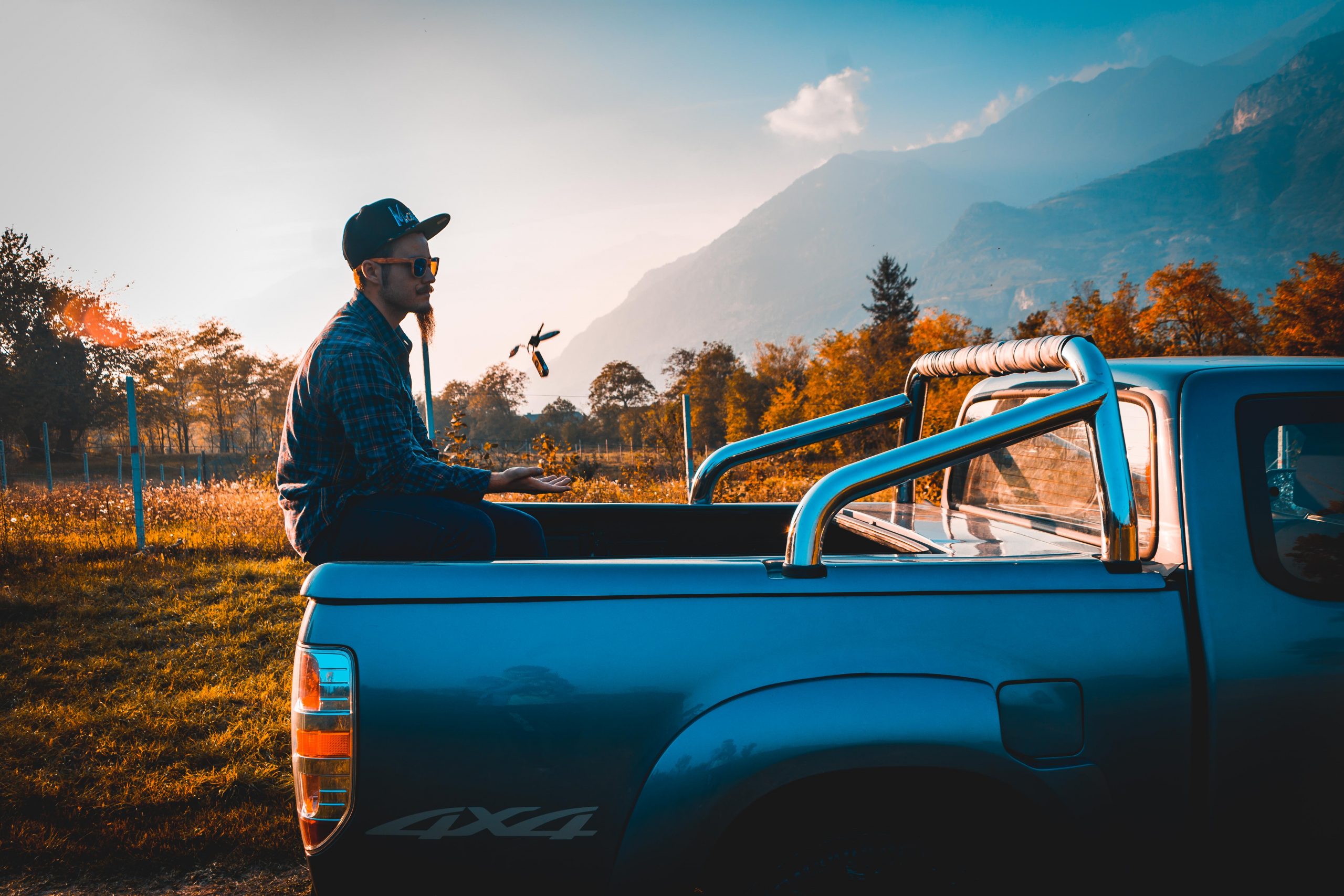 A guy sitting in a pickup truck's bed in the countryside, playing with it's keys