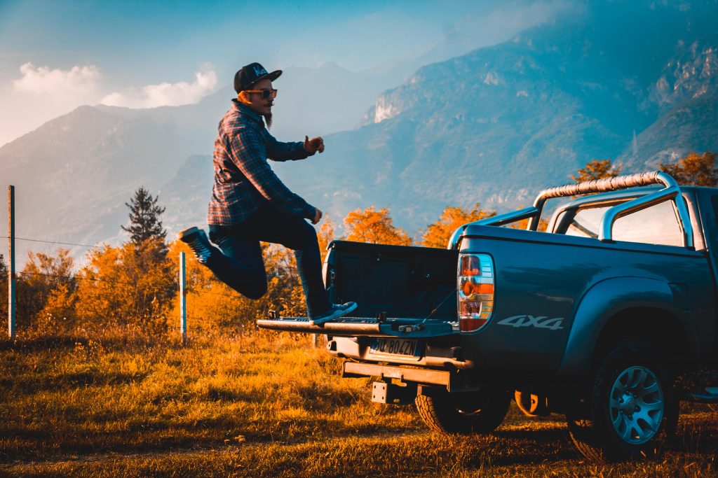 A guy jumping on to a pickup truck's bed