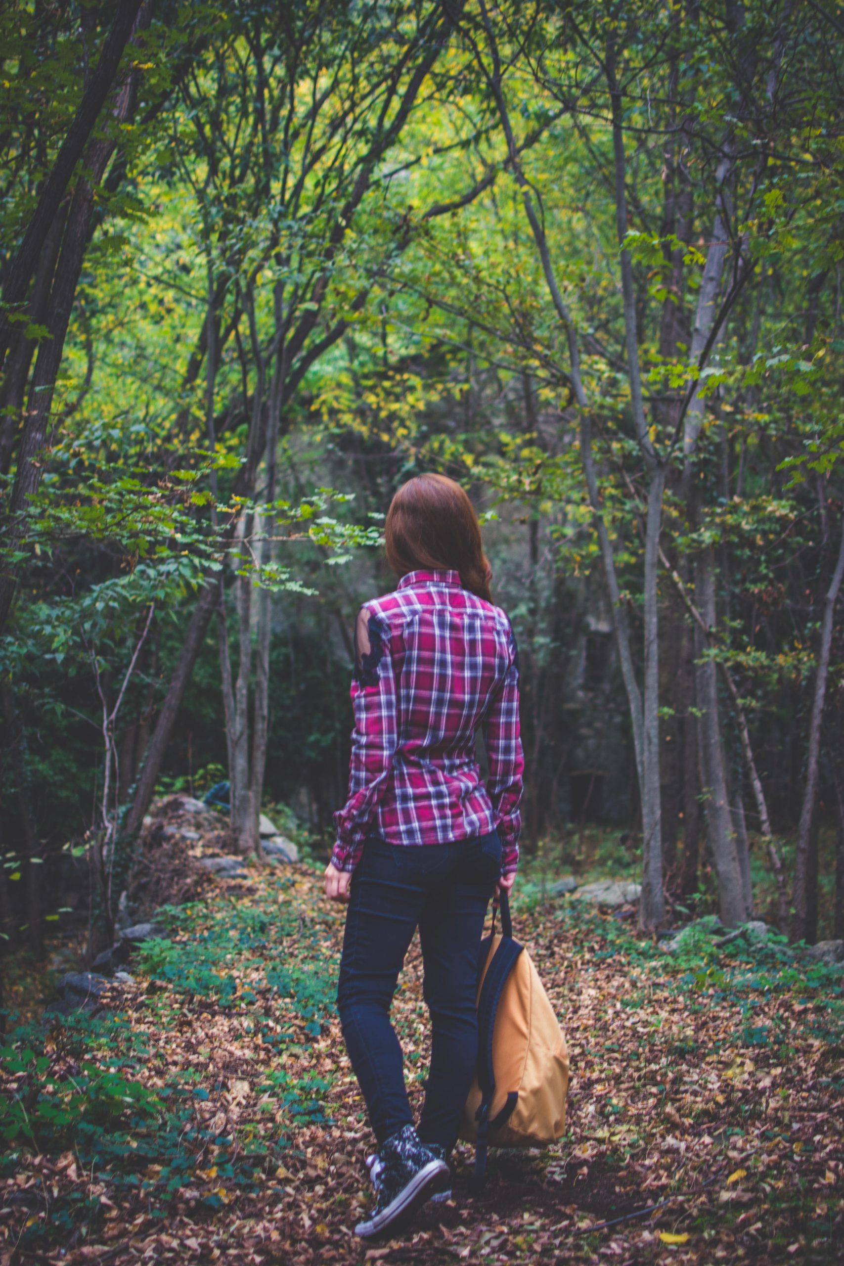 A girl with a orange backpack in her hands standing on a trail in the woods