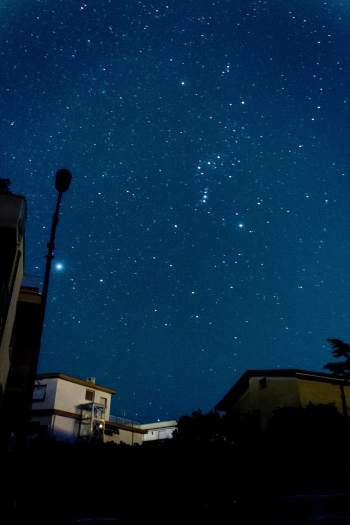 A Sky in the night full of stars with a turned off street lamp and some buildings in the background